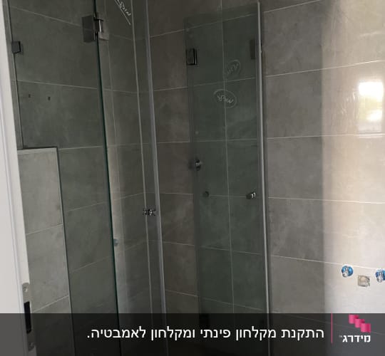 מקלחון זכוכית בחדר אמבטיה עם אריחים אפורים